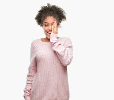 El yüz ve sürpriz duygu kendinden emin gülümseme ile tek gözüyle kapsayan izole arka plan üzerinde kış kazak giyen genç afro Amerikan kadın.