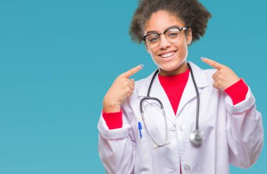 Genç afro Amerikalı doktor kadın kendinden emin gösterilen ve işaret parmakları diş ve ağız ile gülümseyen izole arka plan yüzünden. Sağlık kavramı.