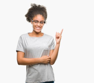 Kameraya bakarak yan el ve parmak ile işaret yüzünde kocaman bir gülümseme ile izole arka plan üzerinde gözlük takan genç afro Amerikalı kadın.