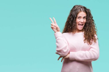 Güzel esmer kıvırcık saçlı Genç kız mutlu yüz zafer işareti yaparken kameraya göz kırpıyor ile gülümseyen izole arka plan üzerinde pembe kış kazak giyiyor. İki numaralı.