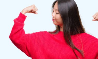 Üzerinde kış kazak giyen genç Asyalı kadın kol kasları gururlu gülümseyen gösterilen arka plan izole. Fitness kavramı.