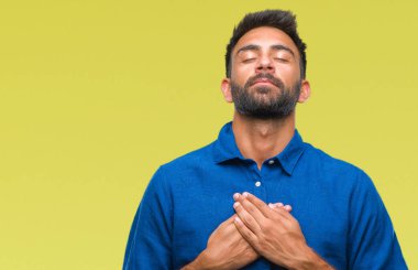 Göğüs kapalı gözler ve yüzünde minnettar jest ile yetişkin İspanyol adam ile gülümseyen izole arka plan üzerinde eller. Sağlık kavramı.