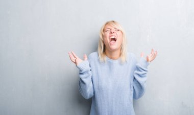 Grunge yetişkin beyaz kadın gri duvar giyen kış kazak kızgın ve çığlık kaldırdı ve kapalı gözleri heyecanlı silah ile başarı için deli kutluyor. Kazanan kavramı