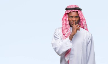 Dudaklarında parmak ile sessiz olmanı izole arka plan üzerinde geleneksel keffiyeh giyen genç Arapça Afrika adam. Sessizlik ve gizli kavramı.