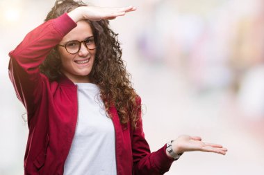 Arka plan eller eller büyük gösterilen ve büyük boy işareti, ölçü birimi sembolü ile genç kız üzerinde ceket ve gözlük takıyor izole güzel esmer kıvırcık saçlı. Kameraya bakarak gülümsüyordu. Ölçüm kavramı.