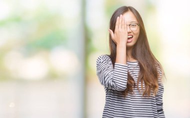 El yüz ve sürpriz duygu kendinden emin gülümseme ile tek gözüyle kapsayan izole arka plan üzerinde gözlük takan Genç Asyalı kadın.