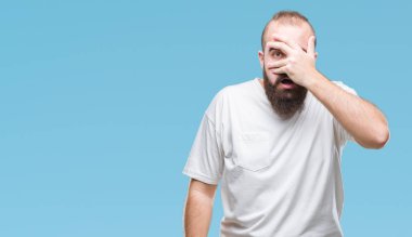 Yüz ve gözler el ile kapsayan şok izole arka plan bakmak üzerinde rahat t-shirt giyen genç beyaz hipster adam utanç ifadesi ile parmaklarımın arasından bakan.