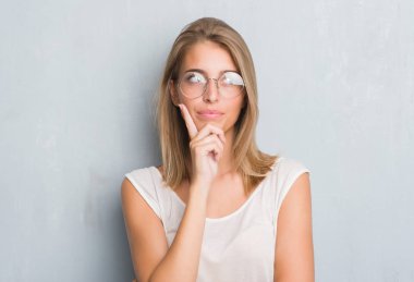 Gözlük ciddi bir yüz düşünme hakkında soru, çok karışık fikir giyen grunge gri duvar üzerinde duran güzel genç kadın