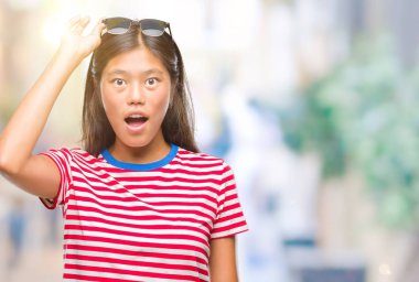 Genç Asyalı kadın korkuyor ve şok sürpriz ifade, korku ve heyecan yüz ile izole arka plan üzerinde güneş gözlüğü takıyor.