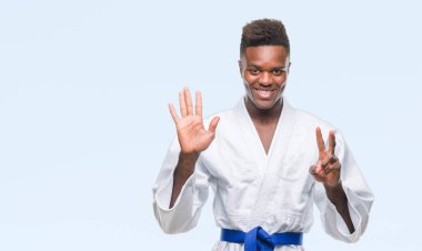 İzole arka planda gösterilen ve parmakları ile işaret kimono giyen genç Afro-Amerikan adam kendinden emin ve mutlu gülümseyerek süre yedi numara.