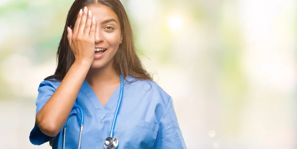 顔と驚きの感情に自信を持って笑顔で手で片目を覆う孤立の背景の上の若いアラブ医師外科医女 — ストック写真