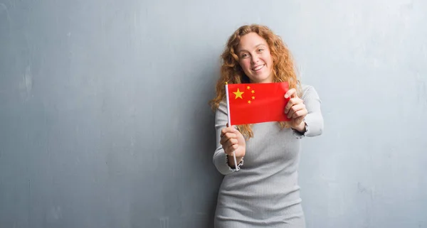 Молодая Рыжая Женщина Над Серой Гранж Стеной Держит Флаг Китая — стоковое фото