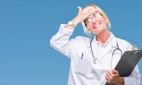 Middle age blonde doctor woman holding clipboard over isolated background stressed with hand on head, shocked with shame and surprise face, angry and frustrated. Fear and upset for mistake.