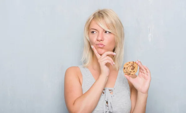 チョコレートを灰色のグランジの壁を食べる以上の白人アダルト女性クッキー深刻な顔を考えて質問 非常に混乱して考え — ストック写真