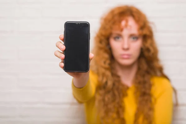 Jovem Ruiva Sentada Sobre Parede Tijolo Mostrando Smartphone Com Uma — Fotografia de Stock