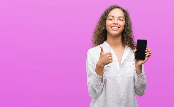 年轻的西班牙裔妇女使用智能手机高兴与大微笑做 拇指与手指 优秀的标志 — 图库照片