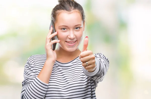 年轻美丽的高加索妇女在智能手机上谈论孤立的背景高兴与大微笑做确定的标志 用手指竖起大拇指 优秀的标志 — 图库照片