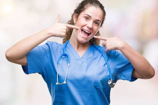 年轻的黑发医生女孩穿着护士或外科医生制服在孤立的背景微笑自信显示和指向用手指牙和嘴 健康理念 — 图库照片