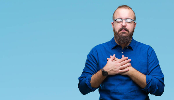 Young caucasian hipster man wearing glasses over isolated background smiling with hands on chest with closed eyes and grateful gesture on face. Health concept.