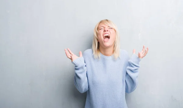 成年白种女人在垃圾灰墙穿冬季毛衣庆祝疯狂和疯狂的成功与胳膊举起和闭着眼睛尖叫兴奋 获奖者概念 — 图库照片