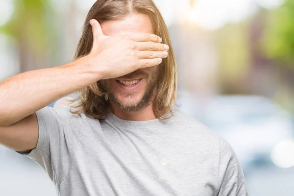 Young handsome man with long hair over isolated background smiling and laughing with hand on face covering eyes for surprise. Blind concept.