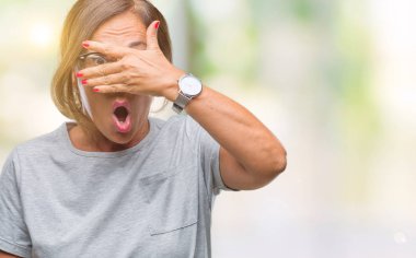 Mahcup ifadeyle parmaklarımın arasından seyir yüz ve gözler el ile kapsayan şok bakmak izole arka plan üzerinde gözlük takan orta yaş İspanyol kadın kıdemli.