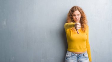 Mutsuz ve kızgın ret gösterilen ve başparmak aşağı hareketi ile negatif seyir gri grunge duvarın üzerinden genç Kızıl saçlı kadın. Kötü ifade.