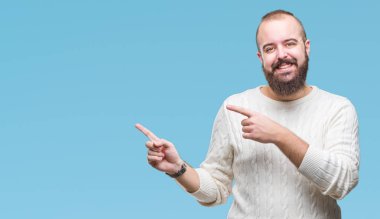 Gülümseyen ve iki elleri ve parmakları ile tarafına işaret kamera bakarak izole arka plan üzerinde kış kazak giyen genç beyaz hipster adam.