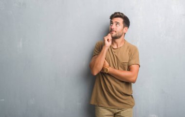 Yakışıklı genç gri grunge duvarın çene düşünme hakkında soru, dalgın ifade üzerine el ile üzerinden. Düşünceli yüzüyle gülümsüyor. Şüphe kavramı.