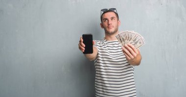 Dolar ve smarphone tutan gri grunge duvarın üzerinden beyaz delikanlı 