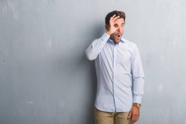 Yakışıklı genç iş adamı ok jest yapıyor şık gömlek giymiş gri grunge duvarın üzerinden sürpriz yüz, göz parmaklarının arasından seyir ile şok. İmansız ifade.