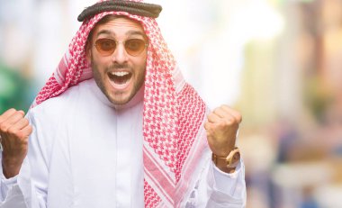 Keffiyeh izole arka plan kutlama üzerinde giyen genç yakışıklı adam şaşırttı ve başarı için kaldırdı kollarını açarak hayret ve gözleri açık. Kazanan kavramı.