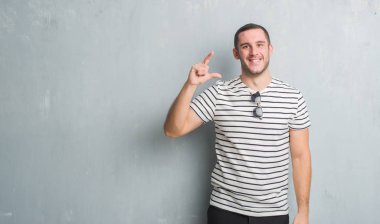 Beyaz delikanlı duvar gri grunge gülümseyen ve süre seyir ve kamera boyutu işaret parmaklarıyla yapıyor el ile kendinden emin eller üzerinde. Ölçü kavramı.