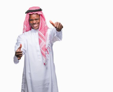 Geleneksel keffiyeh el ile pozitif jest yapıyor onaylama izole arka plan üzerinde giyen genç Arapça Afrika adam başparmak gülümseyen ve başarı için mutlu. Kamera, kazanan jest arıyorsunuz.
