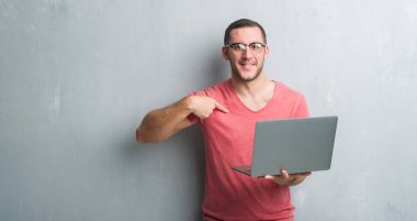 Sürpriz yüz işaret parmağı kendisine bilgisayar dizüstü kullanarak gri grunge duvar üzerinde beyaz delikanlı