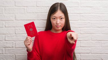 Genç Çinli kadın pasaport Japonya parmak ile kamera ve size işaret tutan tuğla duvarın üzerinden el işareti, pozitif ve kendinden emin bir jest ön