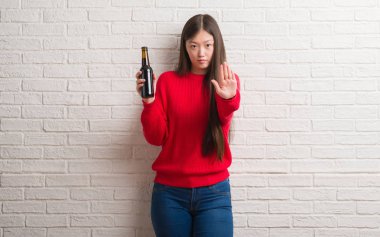 Genç Çinli kadın açık eliyle dur işareti ile ciddi ve kendine güvenen ifade, savunma hareketi yaparken bira içme tuğla duvarın üzerinden