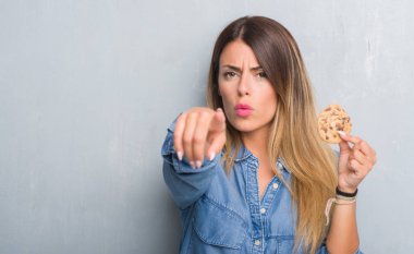 Genç Yetişkin kadın kamera ve size parmak ile işaret çikolatalı bisküvi yemek gri grunge duvarın üzerinden, el işareti, pozitif ve kendinden emin bir jest ön
