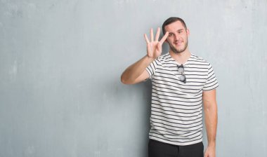 Beyaz delikanlı gösterilen ve parmakları ile işaret gri grunge duvarın üzerinden dört kendinden emin ve mutlu gülümseyerek iken numara.