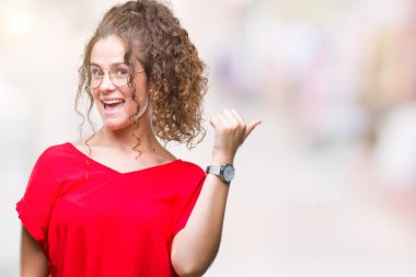 Güzel esmer kıvırcık saçlı Genç kız arıyorum ve başparmak yanında yukarıyı mutlu yüz ile gülümseyen izole arka plan üzerinde gözlük.