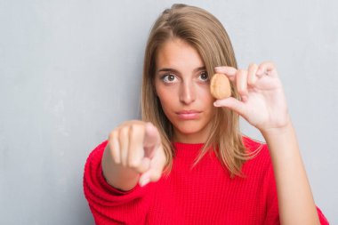 Güzel genç kadın ceviz kamera ve size parmak ile işaret tutan grunge gri duvarın üzerinden ayakta, el işareti, pozitif ve kendinden emin bir jest ön