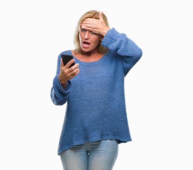 Orta yaş sarışın kadın baş, el ile vurguladı izole arka plan üzerinde Smartphone kullanarak ileti gönderme şok utanç ve sürpriz suratla, öfkeli ve sinirli. Korku ve hata için üzgün.