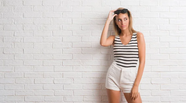 Jovem Mulher Loira Bonita Sobre Parede Tijolo Branco Sorrindo Lado — Fotografia de Stock