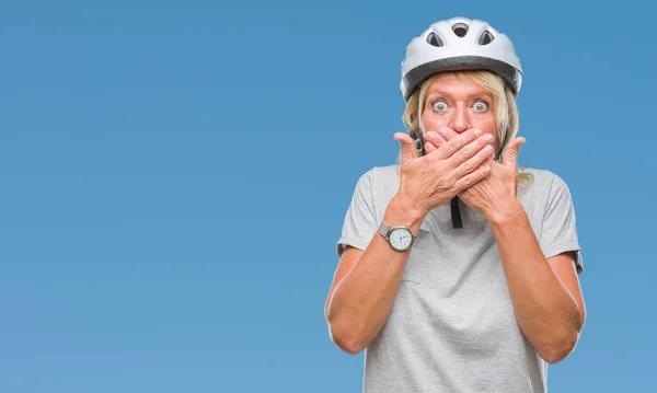 Middle age caucasian cyclist woman wearing safety helmet over isolated background shocked covering mouth with hands for mistake. Secret concept.