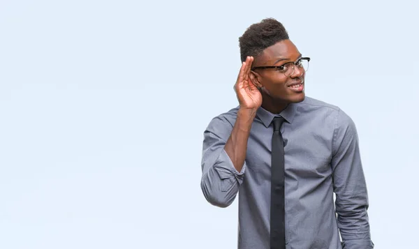Young african american business man over isolated background smiling with hand over ear listening an hearing to rumor or gossip. Deafness concept.