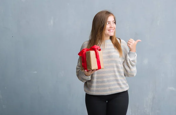 Joven Mujer Adulta Sobre Pared Grunge Gris Sosteniendo Regalo Señalando —  Fotos de Stock