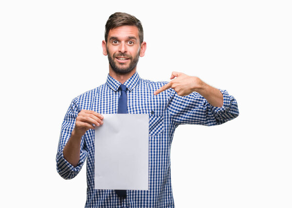 Young handsome man holding blank paper over isolated background with surprise face pointing finger to himself