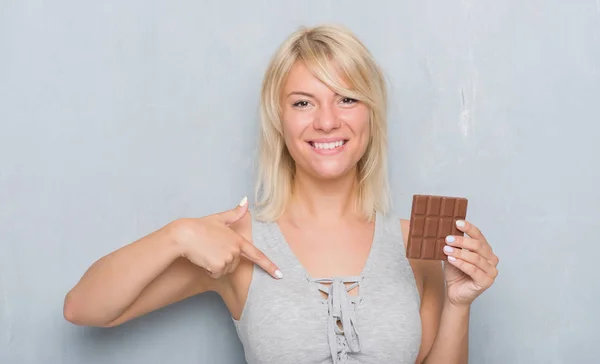 灰色グランジ壁自分自身に驚き顔ポインティング指でバー チョコレートを食べることを白人の大人の女 — ストック写真