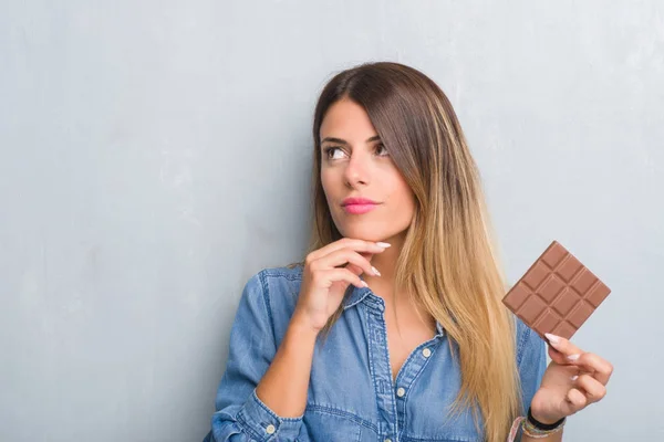 Junge Erwachsene Frau Über Graue Grunge Wand Die Schokoriegel Isst — Stockfoto