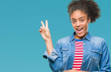 Mutlu yüz zafer işareti yaparken kameraya göz kırpıyor ile gülümseyen izole arka plan üzerinde genç afro Amerikalı kadın. İki numaralı.